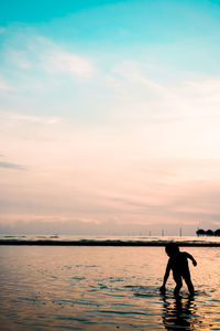 Silhouette men standing in sea against sky during sunset