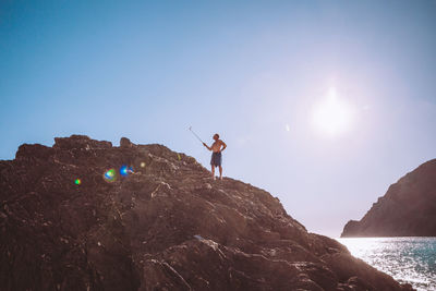 Man standing on rock by sea against sky