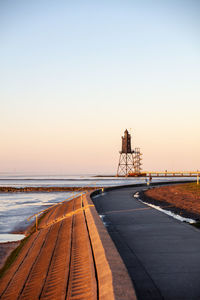 Diminishing perspective of road by sea against clear sky during sunset