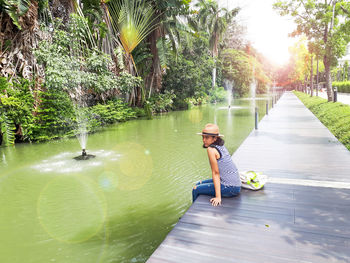 Woman sitting by lake against trees