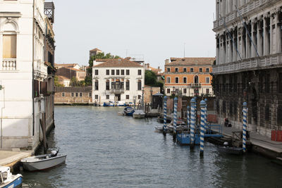 Boats moored in canal amidst buildings in city against clear sky