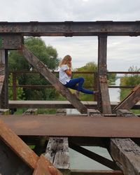 Woman sitting on bridge against sky