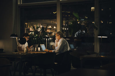 Male and female professionals working late in dark office at night