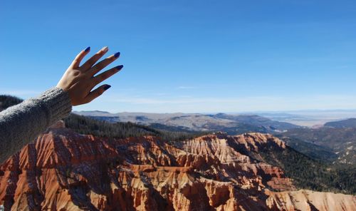 Cropped hand of woman reaching sky over mountains