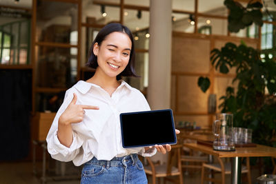 Portrait of young woman using digital tablet while standing in cafe