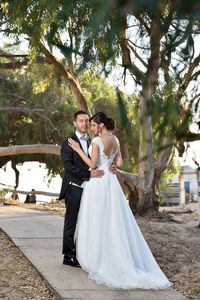 Rear view of couple holding hands while standing by tree