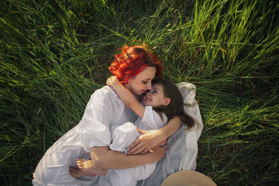 Girl a child hug mother mother with red hair lying on a green field at sunset