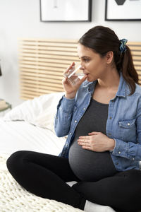 Pregnant woman drinking water sitting on bed