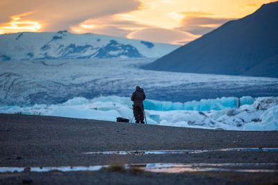 Man standing on snowcapped mountain against sky during sunset