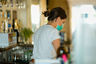 Female barista at work wearing surgical portection face mask to