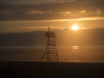 Silhouette crane on beach against sky during sunset