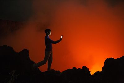 Silhouette of woman photographing volcanic eruption
