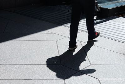 Low section of man walking on sidewalk in city during sunny day