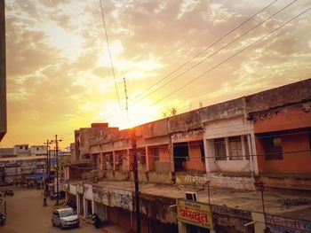 Cars on street by buildings against sky during sunset