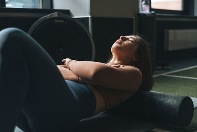 Young brunette woman doing stretching pilates on massage roll in fitness club gym
