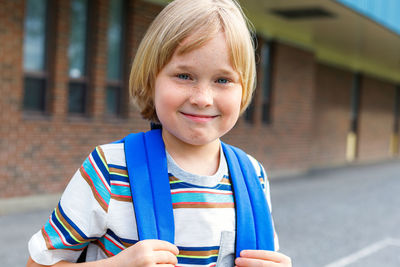 Portrait of smiling boy with backpack near school