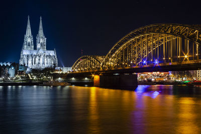 Illuminated bridge over river in city at night