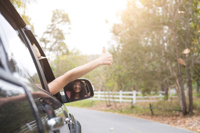 Cropped hand of woman gesturing thumbs up sign in car