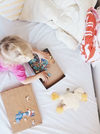High angle view of girl playing jigsaw puzzle on bed