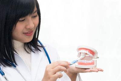 Smiling dentist showing dental mould with toothbrush against white background