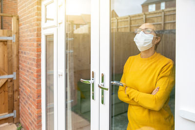 Woman wearing mask standing by window at home