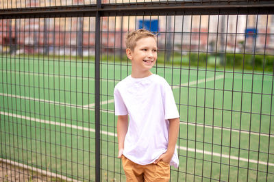 The boy stands at the fence and looks away person