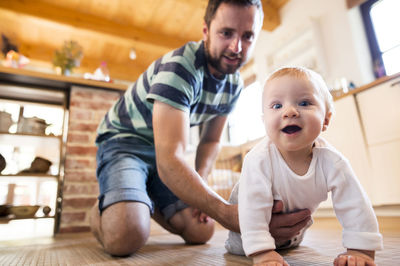 Father supporting crawling baby at home