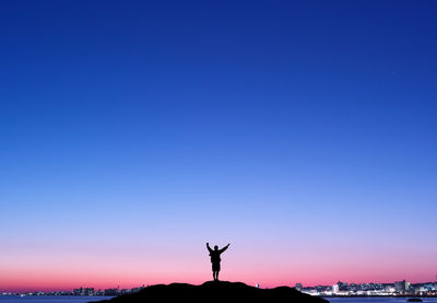 Silhouette person with arms raised on hill against clear blue sky