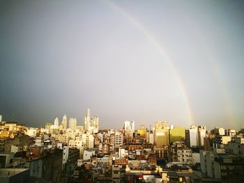 Rainbow over city buildings against clear sky