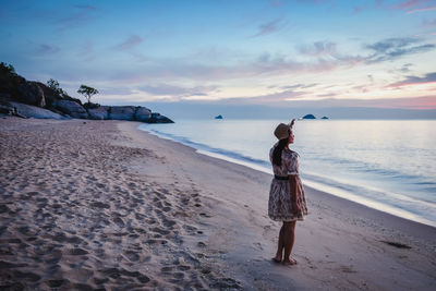 Woman standing on beach against sky during sunset