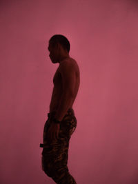 Side view of shirtless man against pink background