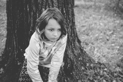 Thoughtful girl bending against tree