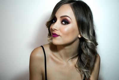 Close-up portrait of beautiful young woman wearing make-up against wall