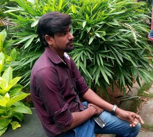 Young man looking away while sitting on plant