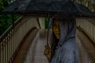 Portrait of woman holding umbrella standing in rain