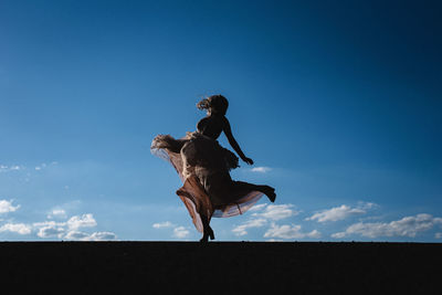 Low angle view of woman jumping against blue sky