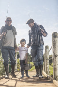 Grandfather, father and son walking over bridge with fishing equipment