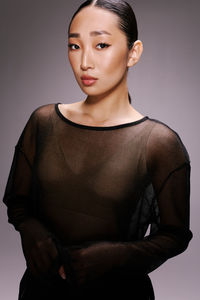 Portrait of young woman standing against gray background
