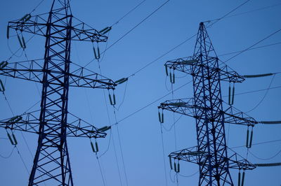 Low angle view of electricity pylon against clear blue sky