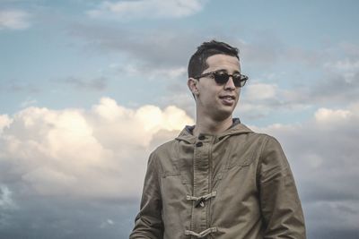 Young man standing against cloudy sky