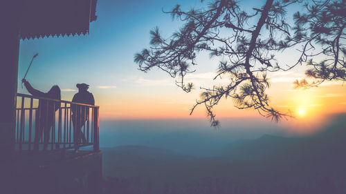 Silhouette person standing by tree against sky during sunset