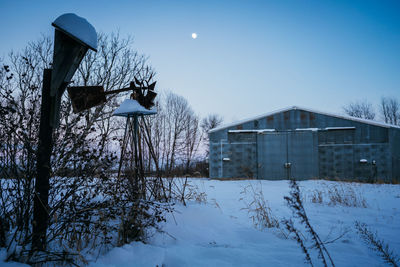 Bare trees by snow covered house against sky