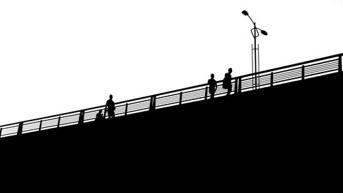 Silhouette people on footbridge against sky
