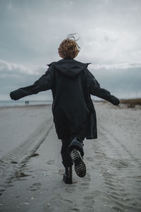 Rear view of woman on beach against sky