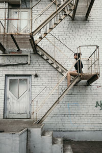 Side view of mid adult woman sitting on staircase against brick wall