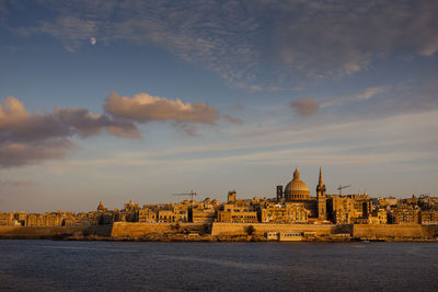 Buildings at waterfront against cloudy sky