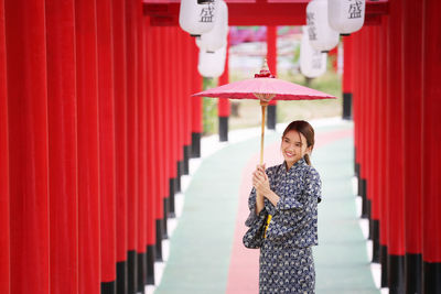 Full length of a smiling young woman standing against red wall