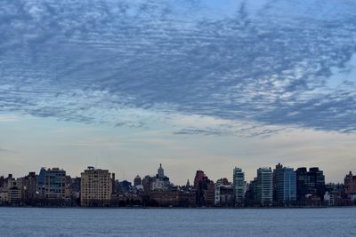 Sea by buildings against sky at dusk