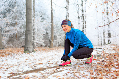 Full length of woman tying shoelace in forest during winter