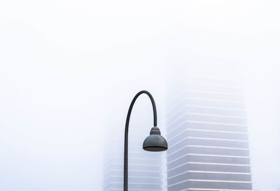 Low angle view of lamp post against buildings during foggy weather